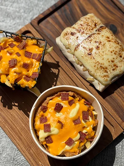 Loaded fries with cheddar and beef bacon next to a gratinated French taco