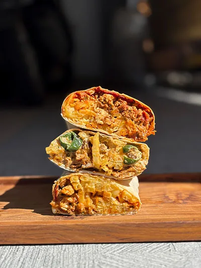 Stack of French tacos cut in half, filled with fries, meat and jalapeños