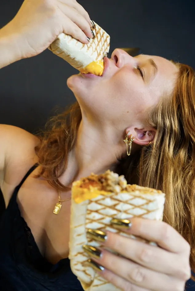 Customer taking a bite of a Bon Appétit French tacos dripping with cheese sauce