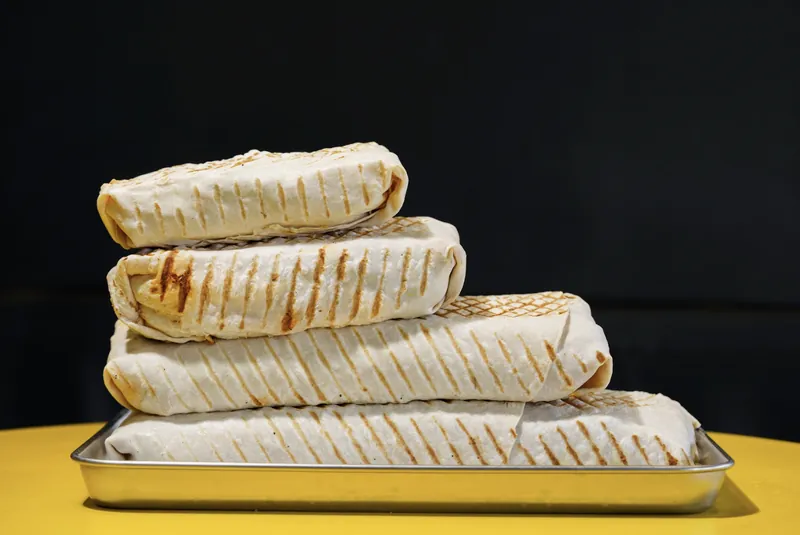 Four grilled Bon Appétit French tacos stacked on a tray, sizes S to XL