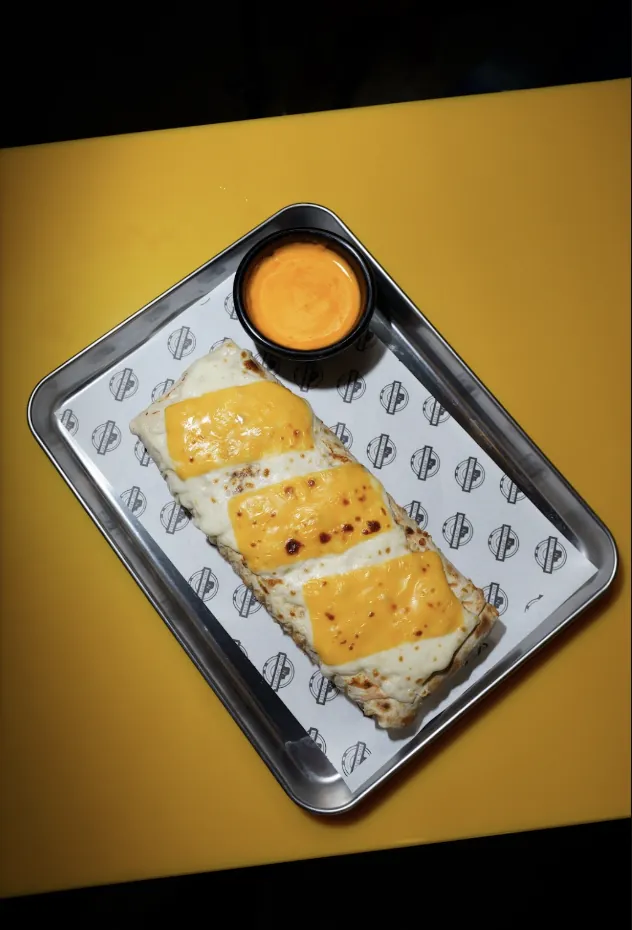 Gratinated French tacos with melted cheese on top and a dipping sauce