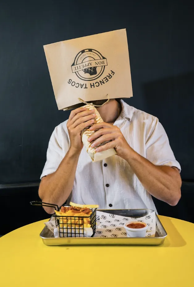 Customer hiding behind a Bon Appétit French tacos paper bag